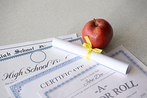 A honor roll recognition, certificate of achievement and high school diploma lies on table with small scroll and red apple. Education documents